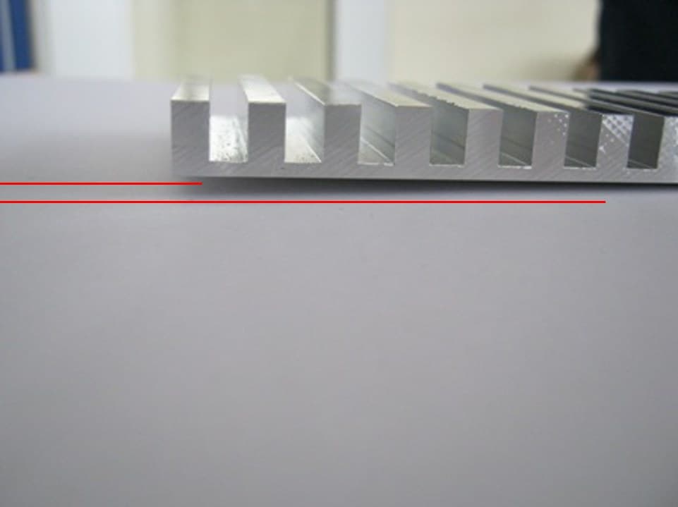 The same comb specimen machined from rolled plate, lifted clear of the reference surface, with the resulting gap marked by red arrows